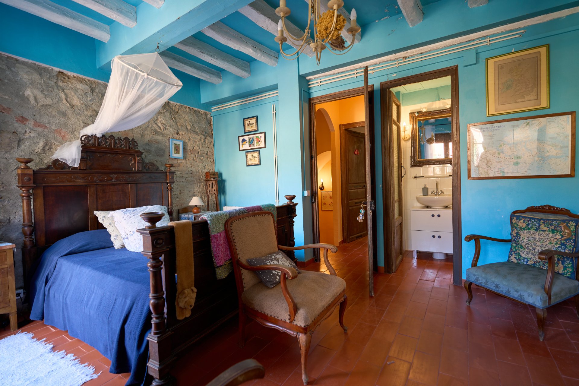 Dormitori d'una casa de poble amb parets blaves i bigues vistes · Objectiu Fotògrafs
