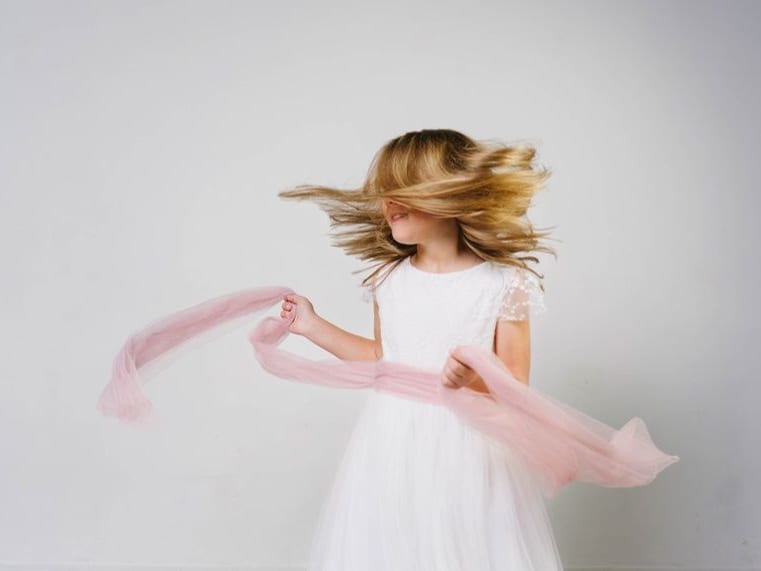 Niña con vestido de comunión haciendo volar el pelo y un pañuelo rosa · Objectiu Fotògrafs, Reus