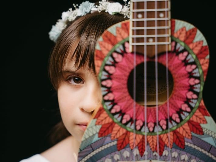 Niña con corona de flores medio escondida detrás de un ukelele pintado · Objectiu Fotògrafs, Reus