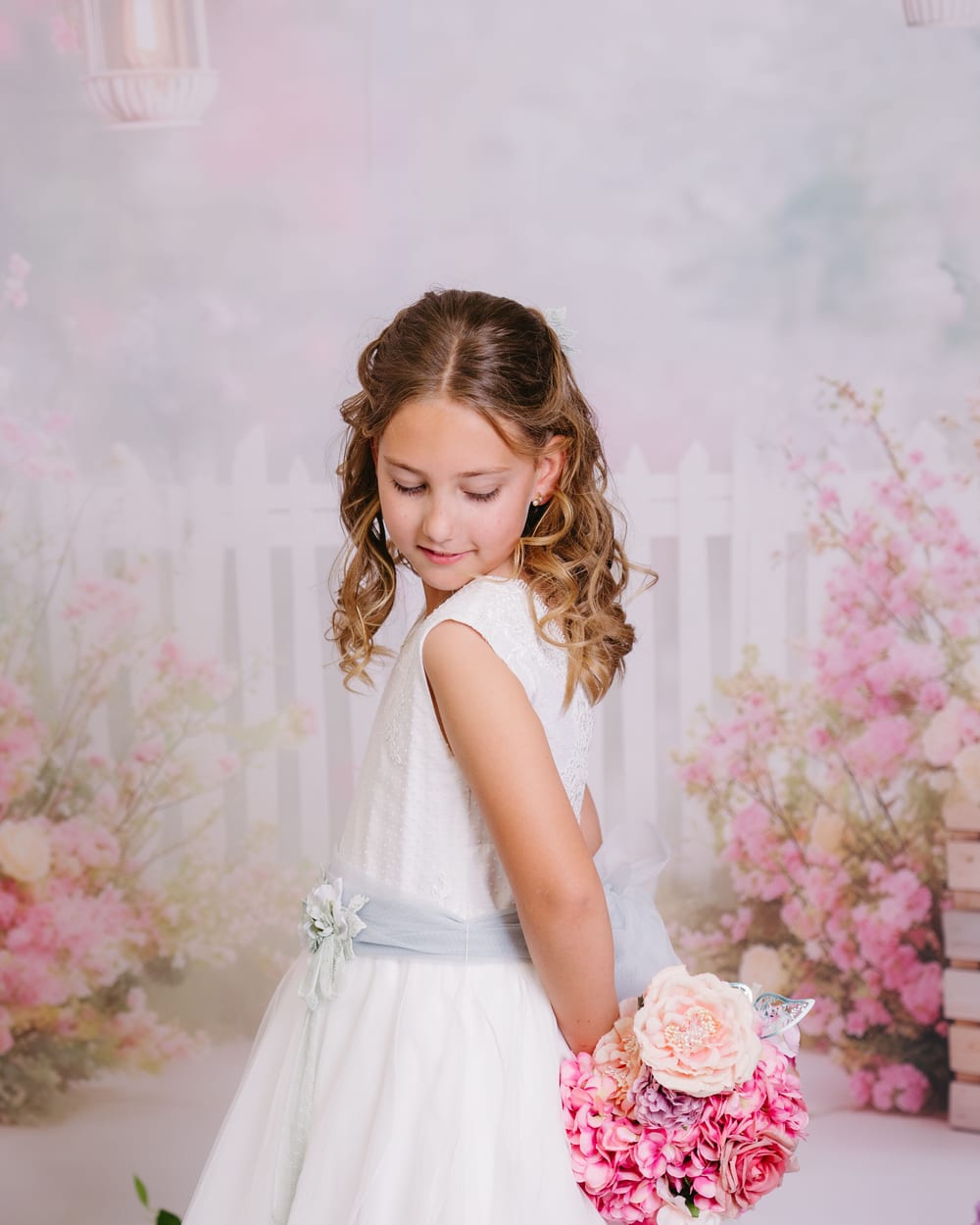 Niña con vestido de comunión y ramo de flores ante un decorado florido · Objectiu Fotògrafs, Reus