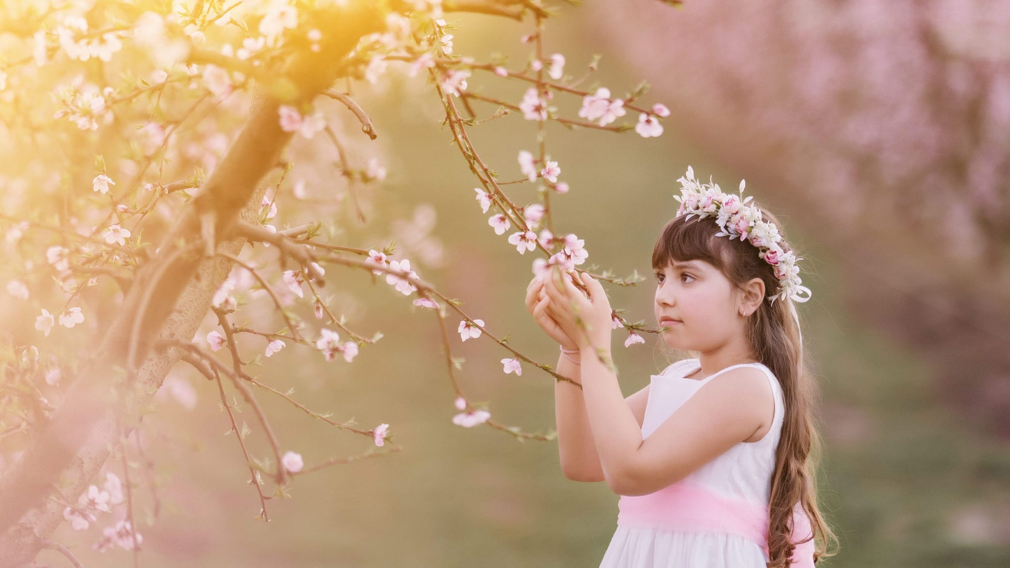 Niña con corona de flores entre árboles en flor en una sesión de comunión en exterior · Objectiu Fotògrafs, Reus