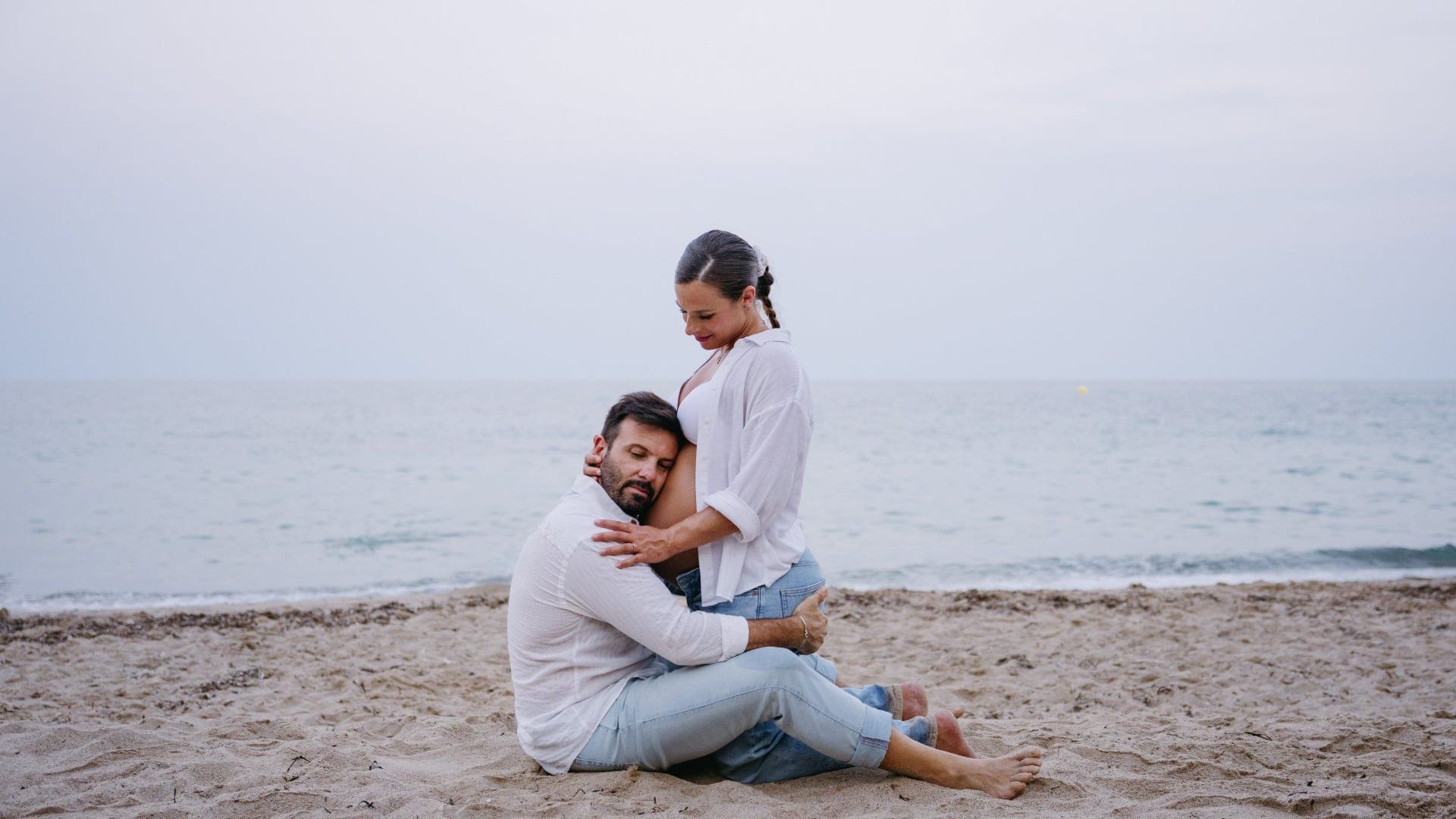 Couple sitting on the beach in a maternity session · Objectiu Fotògrafs, Reus