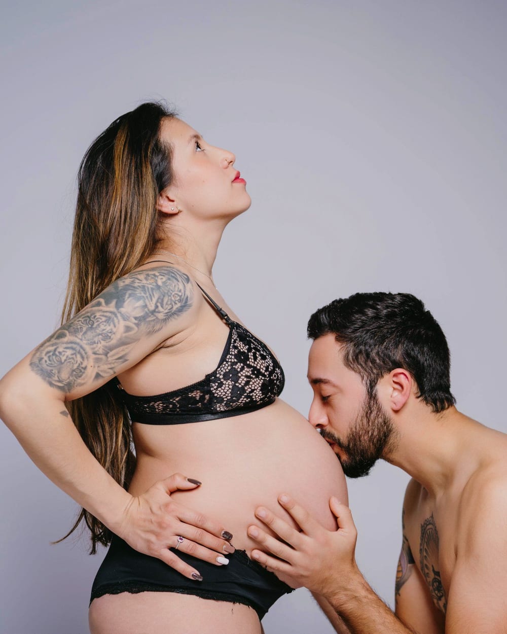 Couple in the studio, him kissing the bump · Objectiu Fotògrafs, Reus