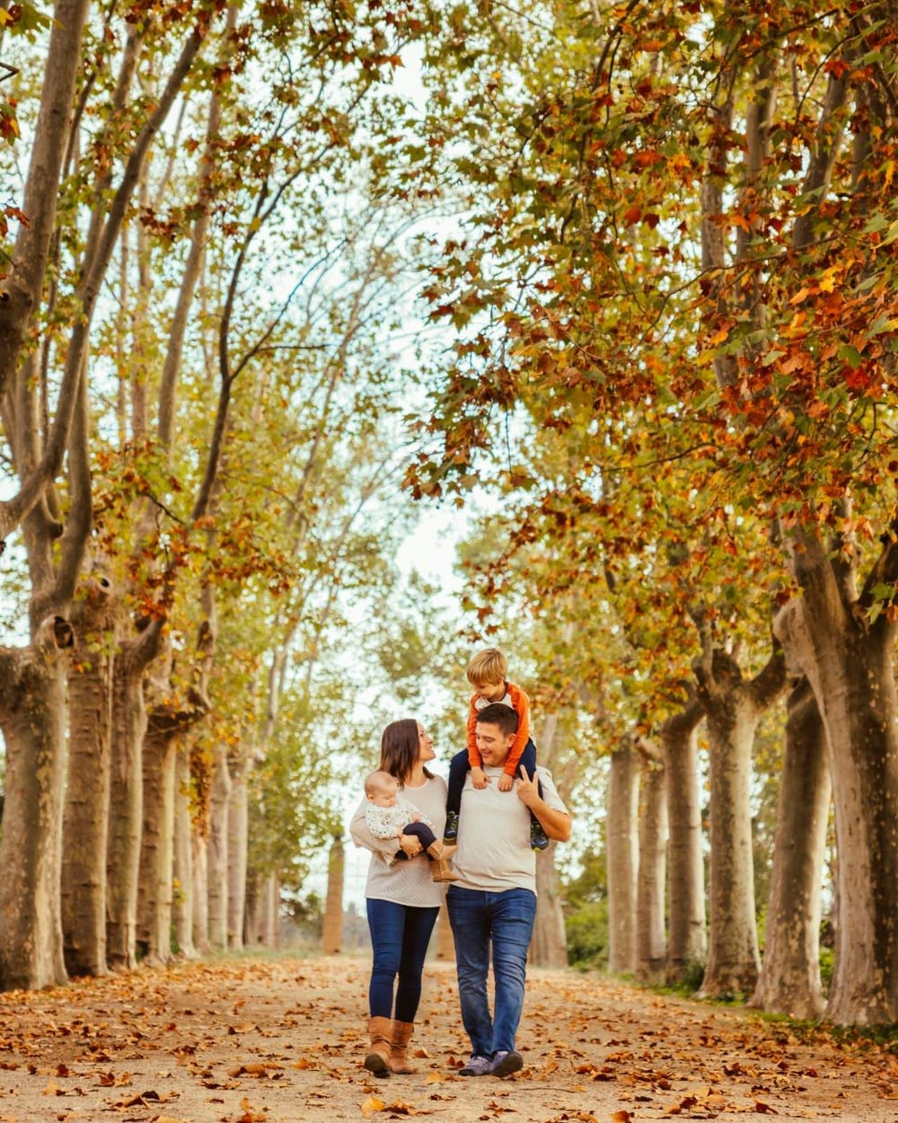 Family walking along a tree-lined avenue in autumn · Objectiu Fotògrafs