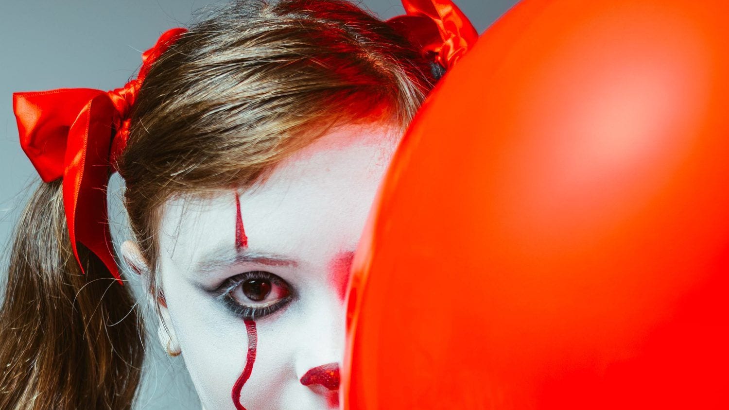 Nena maquillada de pallasso al costat d'un globus vermell en una sessió de Halloween · Objectiu Fotògrafs, Reus