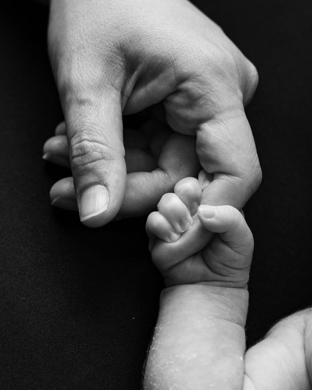 Mano adulta cogiendo la mano de un bebé, en blanco y negro · Objectiu Fotògrafs, Reus
